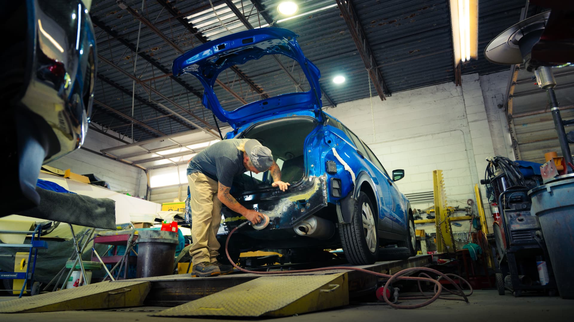 Auto body technician sanding a blue SUV at FL Body Shop in Largo